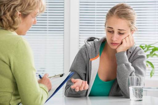 blond teenage girl looking depressed and talking to counsellor